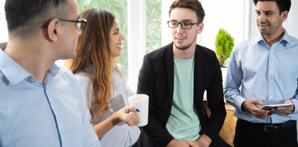 Positive interns sharing training impression. Cheerful young coworkers drinking coffee and chatting. Coffee break or career start concept